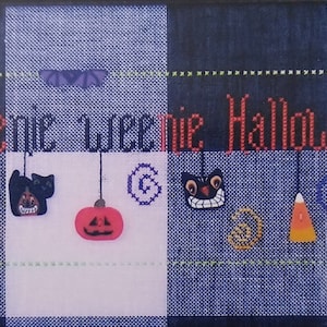 May include: A cross-stitch sampler with the text "a teenie weenie Halloweerie" and various Halloween-themed images, including a skull, a black cat, a pumpkin, a candy corn, and a witch's hat.