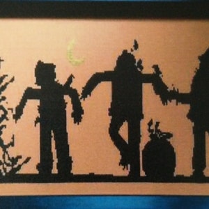 May include: A black and white cross-stitch embroidery depicting three figures in silhouette. The figures are a scarecrow, a witch, and a person holding a pitchfork. The background is a light orange color with a crescent moon.