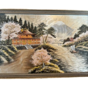 May include: A framed embroidered artwork depicting a Japanese landscape with a traditional temple, cherry blossoms, a river, and Mount Fuji in the background.