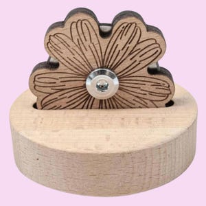 May include: A wooden flower-shaped bottle stopper with a metal screw. The stopper is mounted on a small wooden base.