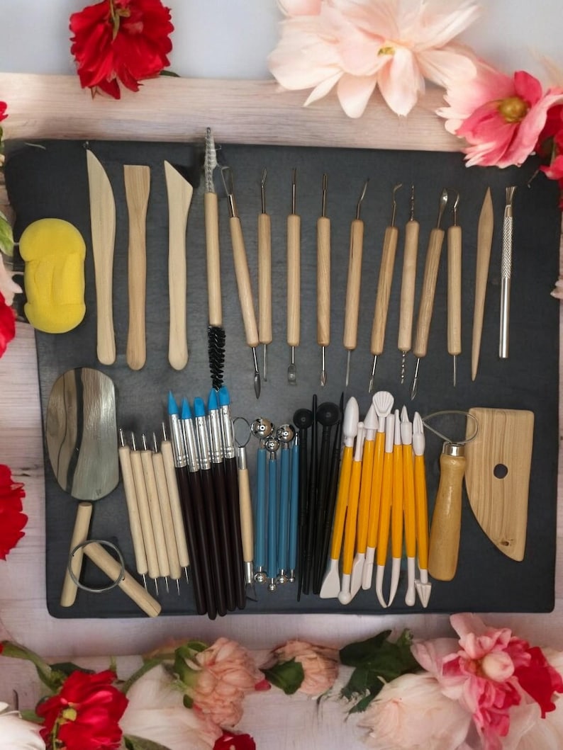 K&ouml;nnte beinhalten: Ein Set mit 30 T&ouml;pfereiger&auml;ten zum Modellieren und Formen von Ton. Die Werkzeuge bestehen aus Holz, Metall und Kunststoff und sind in verschiedenen Formen und Gr&ouml;&szlig;en erh&auml;ltlich. Die Werkzeuge sind auf einer schwarzen Oberfl&auml;che mit einem Schwamm, einem Holzpaddel und einem kleinen Metallschaber angeordnet.