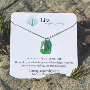 May include: A silver necklace with a green sea glass pendant featuring a turtle design. The pendant is rectangular and hangs from a delicate chain. The card behind the necklace reads "Lita sea glass jewelry" and "-Turtle of Transformation-".