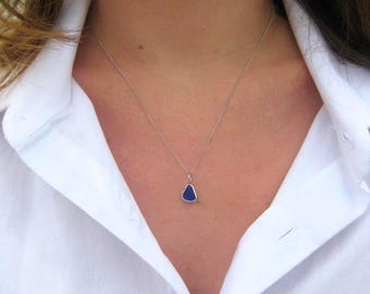 Può includere: Una collana con un piccolo pezzo di vetro marino blu intenso a forma di goccia, sospeso a una sottile catenina in metallo argentato. Il ciondolo è fissato con una semplice contromaglia argentata, dal design essenziale e raffinato.