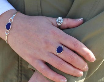 Può includere: Un set di bracciale e anelli in argento con pietre ovali blu scuro. L'anello sull'indice ha una singola pietra, mentre il bracciale ne ha due. È visibile anche un anello a spirale.
