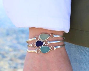 Könnte beinhalten: Drei Armbänder aus Sterlingsilber mit glatten, abgerundeten Meerglasstücken in Hellgrün, Dunkelblau und Meergrün. Jedes Armband ist durch silberne Glieder und Ringe verbunden. Der Text Real Sea Glass . Sterling Silver . ist sichtbar.