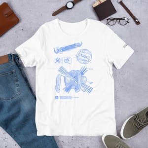May include: White t-shirt featuring a blue blueprint design of a nuclear fusion reactor. The design includes a diagram of a tokamak, a stellarator, and a magnetic coil. The text on the shirt reads "Magnetic Fusion Technology Facility, Lawrence Livermore National Laboratory, University of California".