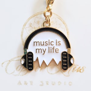 May include: Gold charm featuring a black and white enamel design of headphones with the text "music is my life".