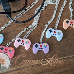 Puede incluir: Siete collares de plata con colgantes de mando de juego de plástico de colores. Los mandos son en tonos de rosa, azul, morado y melocotón. El texto "Copper Lotus" es visible en la parte inferior central de la imagen.