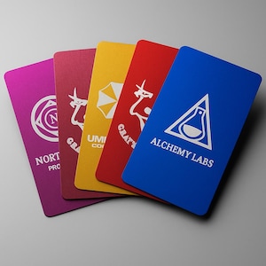 Puede incluir: Un conjunto de cinco tarjetas de visita coloridas. Cada tarjeta presenta un color sólido diferente: magenta, burdeos, amarillo, rojo y azul. Cada tarjeta tiene un logotipo y texto blanco únicos, incluyendo "NORTH PRO" y "ALCHEMY LABS".