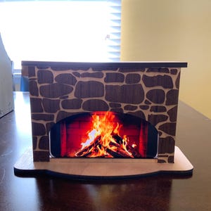 May include: A wooden fireplace mantel with a stone facade and a digital image of a fire inside. The mantel is brown and has a rounded base.