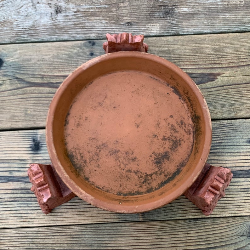 Op de afbeelding: Een terracotta plantenpot met drie decoratieve poten. De pot is bruin en heeft een ruwe textuur.