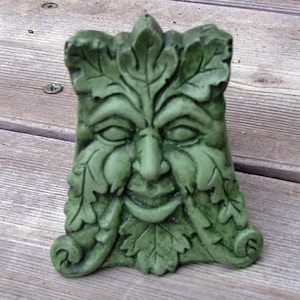 May include: Green man sculpture with a leafy face and a whimsical expression. The sculpture is made of a green material and has a textured surface.