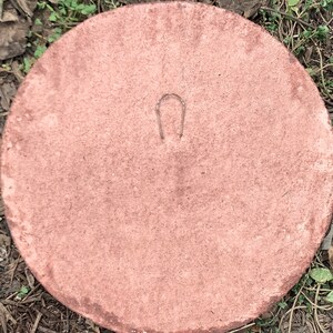 May include: A round, terracotta-colored concrete stepping stone with a small metal loop on the back.