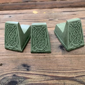 May include: Three green concrete bookends with a Celtic knot design. The bookends are shaped like a wedge and have a raised design on the front.