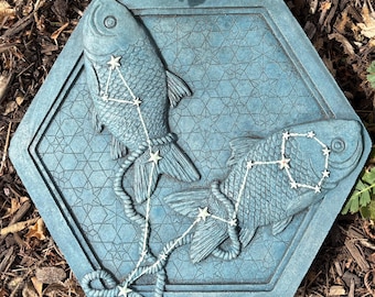 Puede incluir: Una losa hexagonal azul verdoso con dos peces con constelaciones estelares. Los peces están conectados por un diseño similar a una cuerda, y el fondo tiene un patrón geométrico. Adecuado para jardín o patio.