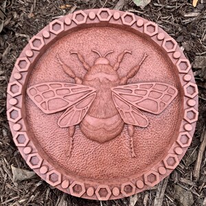 May include: A round, copper-colored wall plaque with a raised, detailed image of a bumblebee. The plaque has a decorative border of hexagons.