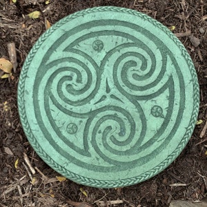 May include: A green circular stepping stone with a Celtic knot design. The stone has a rope-like border.
