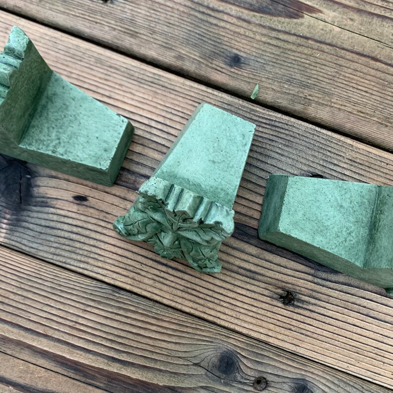 May include: Three green painted wooden corner brackets with decorative carvings. The brackets are on a wooden surface.