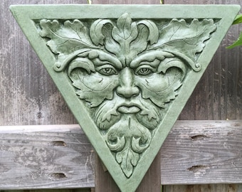 May include: A green, triangular wall plaque with a sculpted face of the Green Man. The face is surrounded by leaves and vines.