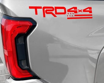 May include: Red TRD 4x4 decal on a silver vehicle. The decal features the TRD logo, the text "4x4", and a design with stars and stripes. The vehicle's red taillight is visible on the left side of the image.