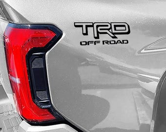 May include: A silver pickup truck with a black "TRD OFF ROAD" emblem on the tailgate.