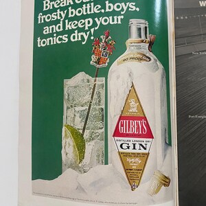 May include: A vintage advertisement for Gilbey's London Dry Gin. The ad features a frosted bottle of gin with a lime wedge and ice in a glass. The text reads "Break out the frosty bottle, boys, and keep your tonics dry!"