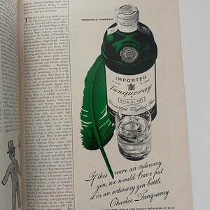 May include: A green bottle of Tanqueray gin with a white label that reads "Imported Tanqueray Special Dry Distilled English Gin". The bottle is sitting on a white background with a green feather pen and a glass of gin.