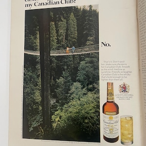 May include: A print advertisement for Canadian Club whisky featuring a couple walking across a suspension bridge in a lush forest. The text reads "Isn't there an easier way to earn my Canadian Club?" and "No." The ad also features a bottle of Canadian Club whisky and a glass of ice with whisky.