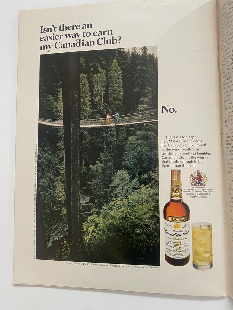 May include: A print advertisement for Canadian Club whisky featuring a couple walking across a suspension bridge in a lush forest. The text reads "Isn't there an easier way to earn my Canadian Club?" and "No." The ad also features a bottle of Canadian Club whisky and a glass of ice with whisky.