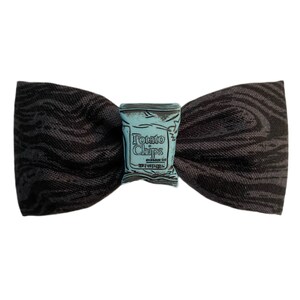 May include: A black bow tie with a blue and white potato chip bag design in the center. The bag has the text "Potato Chips" printed on it.