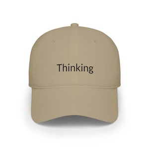 May include: A khaki baseball cap with a structured crown and a curved brim. The front panel features the word Thinking printed in a simple black sans-serif font. The cap is constructed from a solid-colored fabric with a button at the top center.