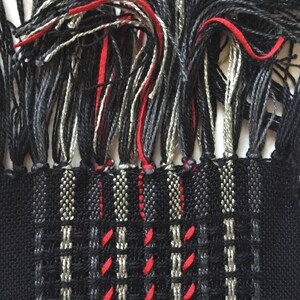 May include: Black and gray woven fabric with red accents. The fabric has a fringe on the top edge.