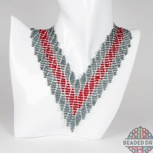 May include: A beaded necklace in a V-shape, displayed on a white mannequin bust. The necklace features a pattern of red and gray beads. The necklace is a handmade jewelry item.