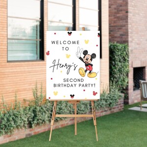 May include: Welcome to Henry's Second Birthday Party sign featuring a cartoon Mickey Mouse in red shorts and yellow shoes, waving with two fingers. The sign has a white background with red and yellow polka dots and Mickey Mouse ears.