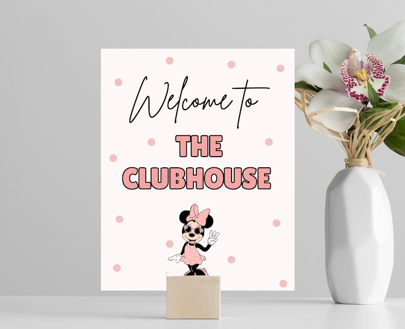 May include: A white sign with pink polka dots and black text that says "Welcome to The Clubhouse". A cartoon image of Minnie Mouse wearing sunglasses and a pink dress is below the text.