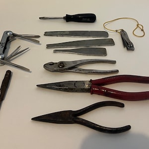 May include: A collection of tools including a multi-tool, a screwdriver, pliers, and a nail clipper. The tools are laid out on a white surface.