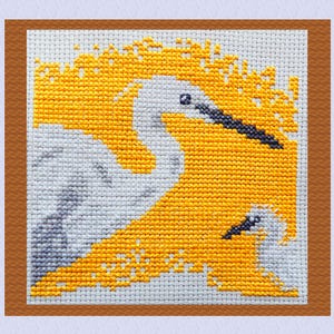 Peut inclure: Broderie au point de croix représentant deux oiseaux blancs avec des becs noirs sur un fond jaune vif. Les oiseaux sont encadrés dans un carré avec une bordure marron. L'œuvre est réalisée avec des points détaillés.