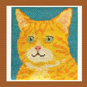 May include: A cross-stitch portrait of a ginger cat with green eyes and a pink nose. The cat's fur is a mix of orange and yellow threads, set against a teal blue background. The artwork is framed in white and brown.