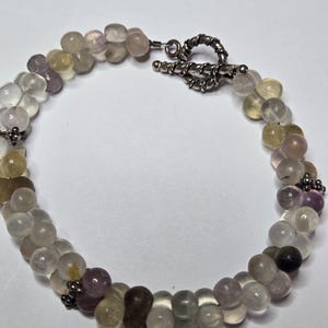 May include: A double-strand bracelet featuring a variety of small, rounded beads in shades of purple, yellow, brown, and clear. The bracelet has a silver-toned toggle clasp. The beads are strung together to create a unique accessory.