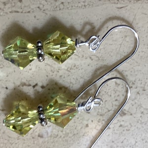 May include: A pair of silver dangle earrings with two light green faceted crystal beads on each earring.