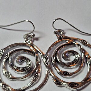 May include: A pair of silver-toned spiral earrings. Each earring features a swirling design with small, oval-shaped cutouts along the curves. The earrings have a hook closure for pierced ears and are set against a white background.