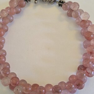 May include: A delicate bracelet featuring strands of round, translucent, pink gemstones. The beads are strung together, forming a braided pattern. The clasp is silver-toned, with a decorative twist design.