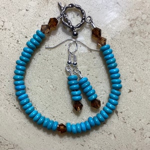 May include: A turquoise beaded bracelet and matching earrings set. The bracelet features round, light blue beads with brown crystal accents and a silver toggle clasp. The earrings have a similar design, with silver hooks.