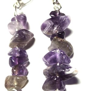 May include: A pair of dangle earrings featuring polished amethyst stones in shades of purple and gray. The stones are strung together with silver-colored metal wire, creating a cascading effect. The earrings have a simple hook closure.
