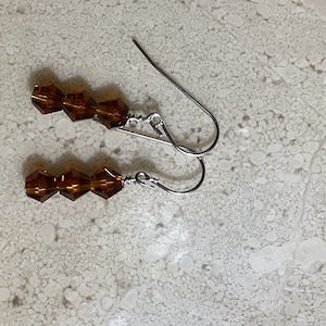 May include: A pair of silver dangle earrings with three amber-colored faceted glass beads on each earring.