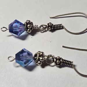 May include: A pair of dangle earrings featuring faceted blue crystal beads. The earrings have silver-colored metal accents, including small ball-shaped details and coiled wire. The ear wires are simple hooks.