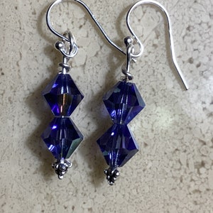 May include: A pair of silver dangle earrings with two dark blue crystal beads on each earring.