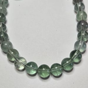 May include: A beaded bracelet featuring translucent green and purple fluorite gemstone beads. The bracelet has a silver-colored toggle clasp. The beads are round and evenly sized, creating a smooth, elegant look. The bracelet is designed for everyday wear.