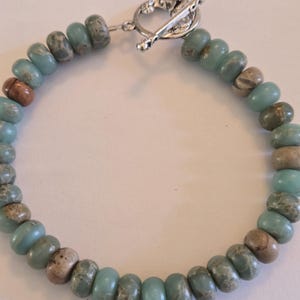 May include: A beaded bracelet featuring a mix of blue, brown, and gray beads. The beads are strung together with a silver-colored clasp. The bracelet is a casual accessory.