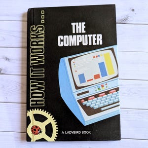 May include: A black hardcover book titled How It Works: The Computer, a Ladybird book. The cover features a light blue vintage computer illustration with a screen displaying a colorful bar graph, a keyboard, and a yellow gear icon with a ladybug.